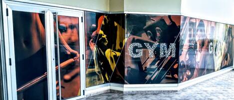 Een gang met betegelde vloer en glazen deuren, voorzien van grote posters over fitness op de muren.