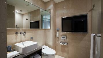 A modern bathroom with a large mirror, a sink, a toilet, and a built-in TV.