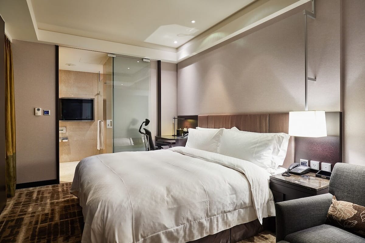 Une chambre d’hôtel avec un grand lit, un bureau avec une lampe, une chaise et un téléviseur.