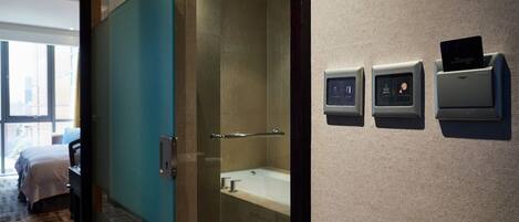 A hotel room with a glass door leading to a bathroom, a bed, and a desk.