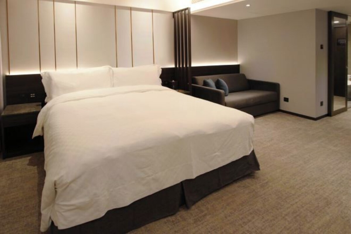 A modern hotel room with a large bed, a seating area, and a walk-in closet.