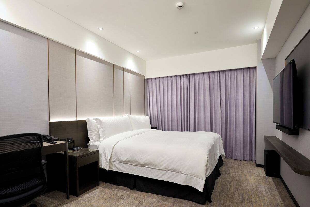 Ein Hotelzimmer mit Bett, Schreibtisch mit Telefon, Stuhl, Fernseher und Vorhang.