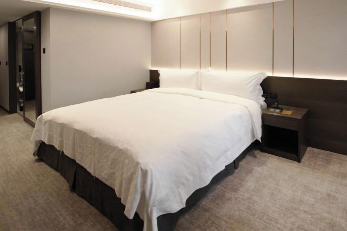 Una habitación de hotel moderna con una cama grande, una mesita de noche y un armario.