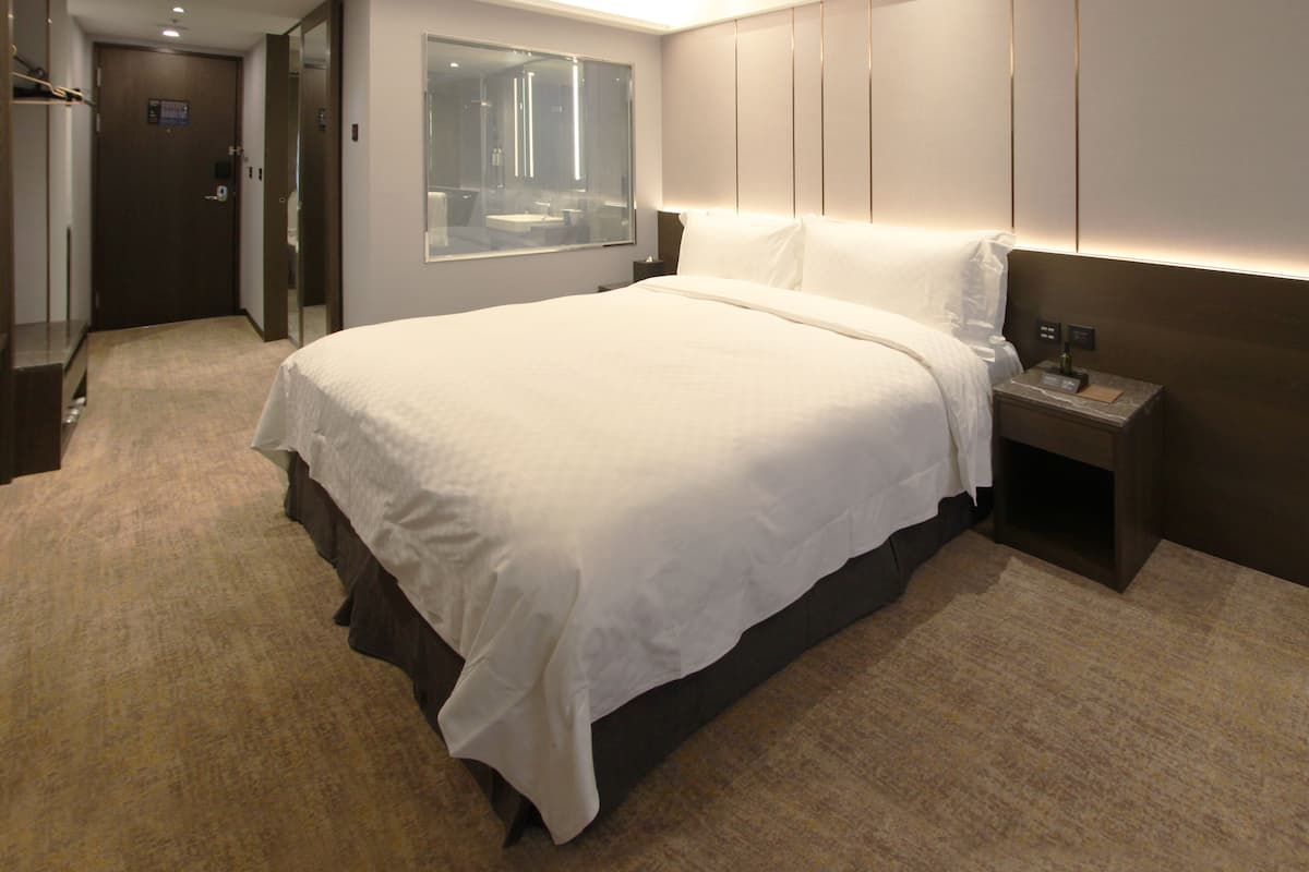 Ein Hotelzimmer mit einem großen Bett, einem Nachttisch, einem Spiegel und einer Tür zu einem Badezimmer.