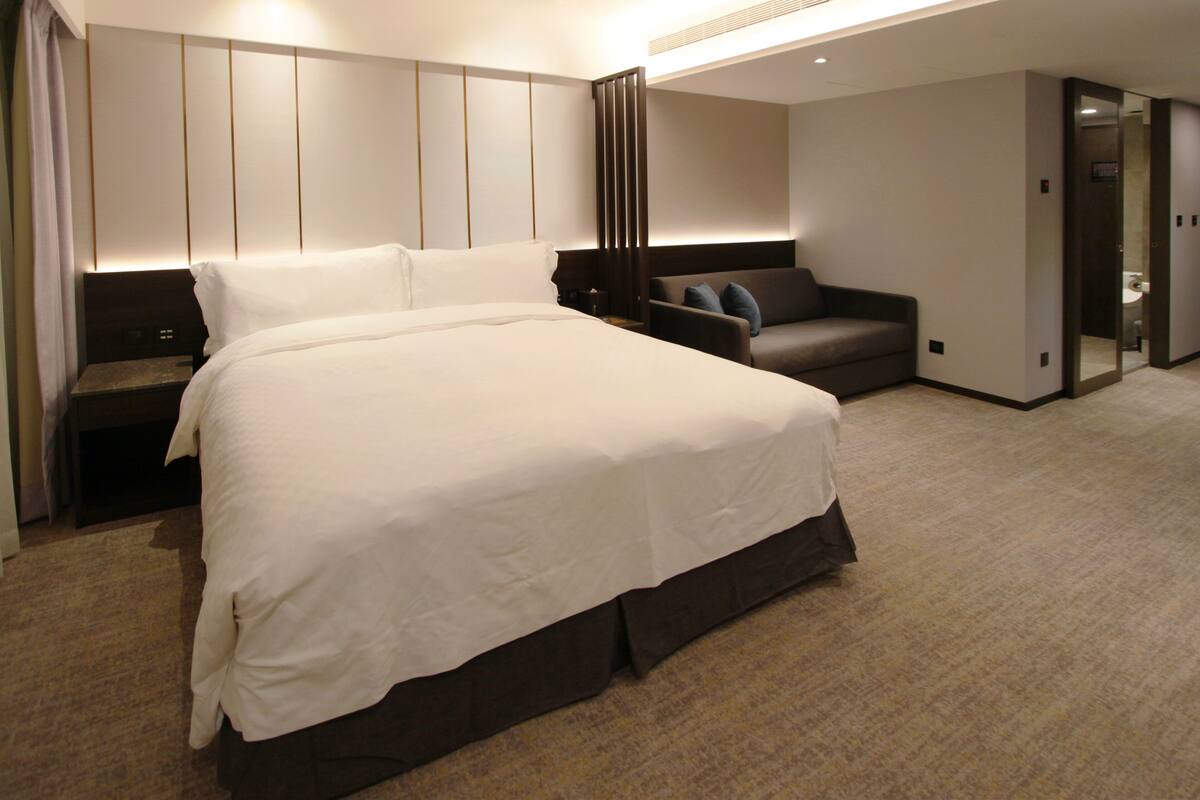 Ein modernes Hotelzimmer mit einem großen Bett, einer Couch, einem Schreibtisch und einem begehbaren Kleiderschrank.