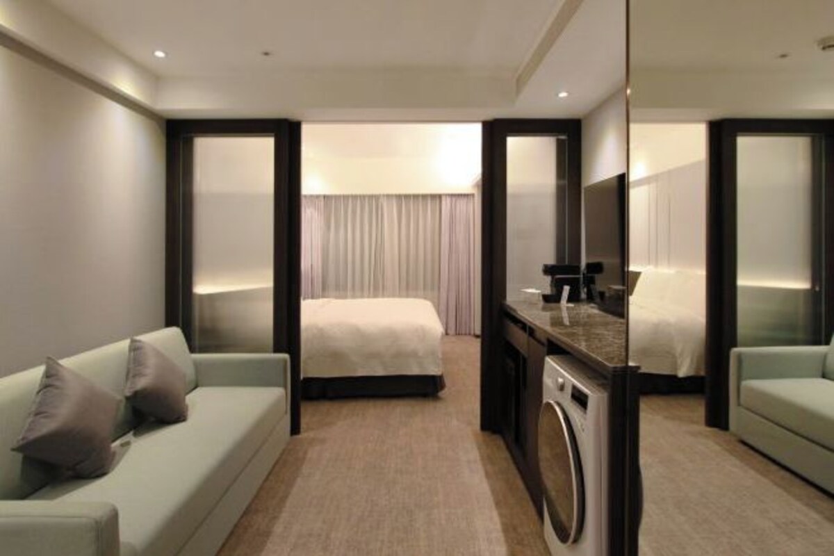 A hotel room with a bed, a sofa, a desk, and a washing machine.