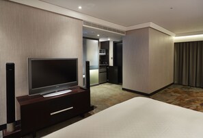 Hotellihuone, jossa on suuri litteänäyttöinen televisio, sänky, tietokoneella varustettu työpöytä ja pieni keittiöalue huoneen takaosassa.