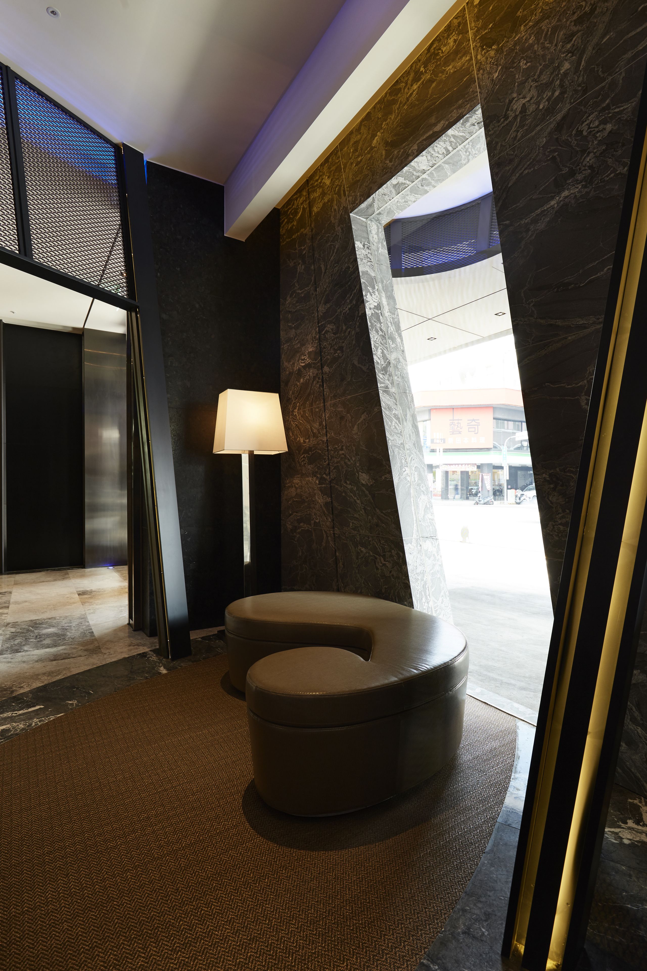 A modern lobby with a curved seating area, a standing lamp, and a view of the street outside.
