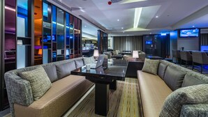Eine moderne Hotelhalle mit einer Sitzecke, ausgestattet mit Sofas und einem Couchtisch, einem Fernseher und einer Glaswand mit farbigem Licht.