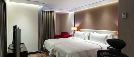 A hotel room with a large bed, a desk with a computer, a red chair, and a TV.