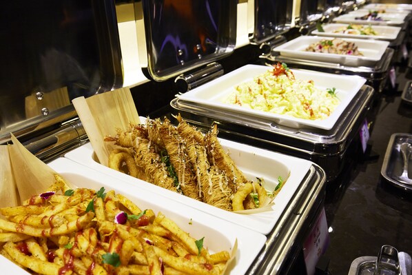 Un bufé con diversos platos, incluyendo papas fritas, fideos y ensaladas.