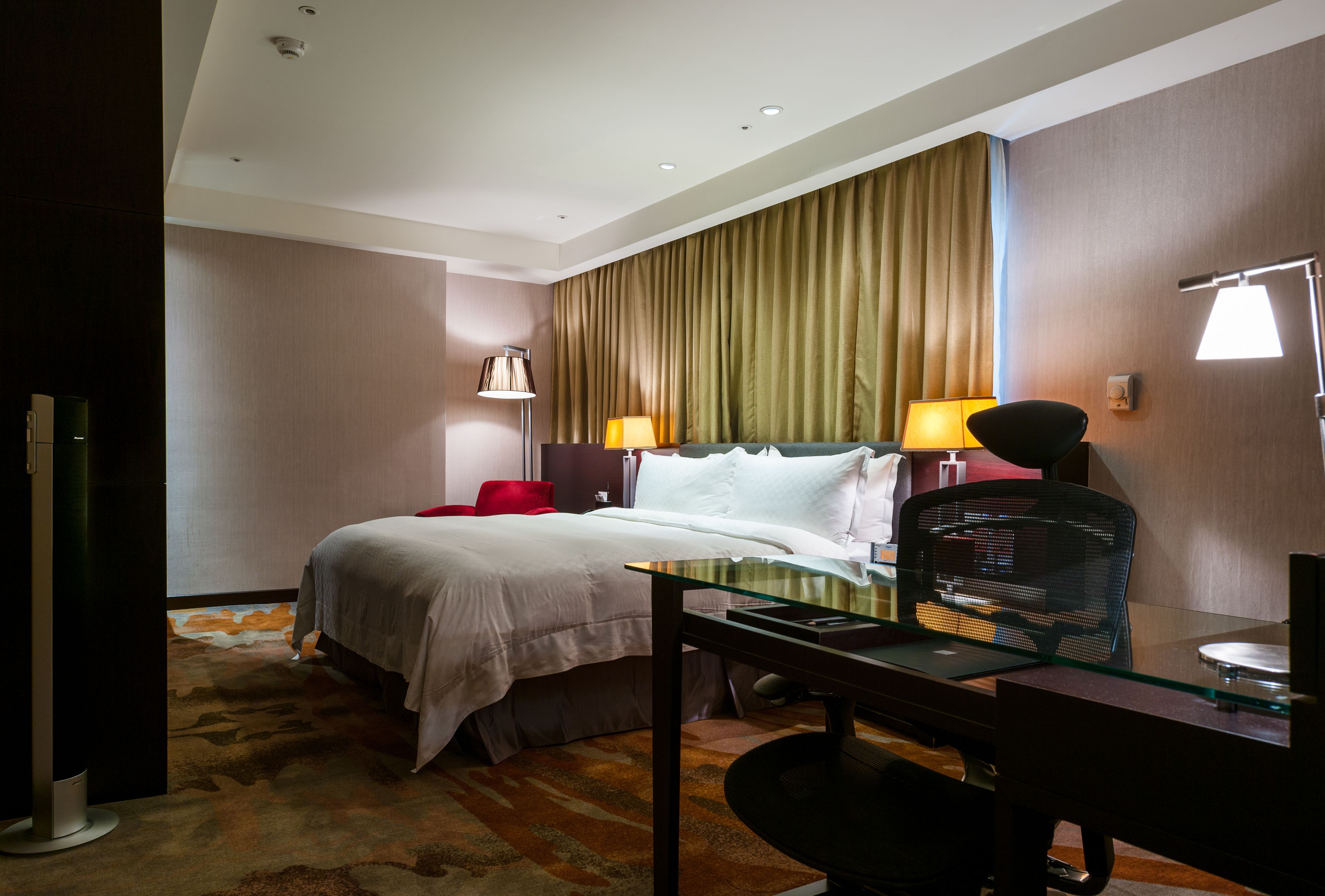 Una habitación de hotel con una cama, un escritorio, una silla y dos lámparas.
