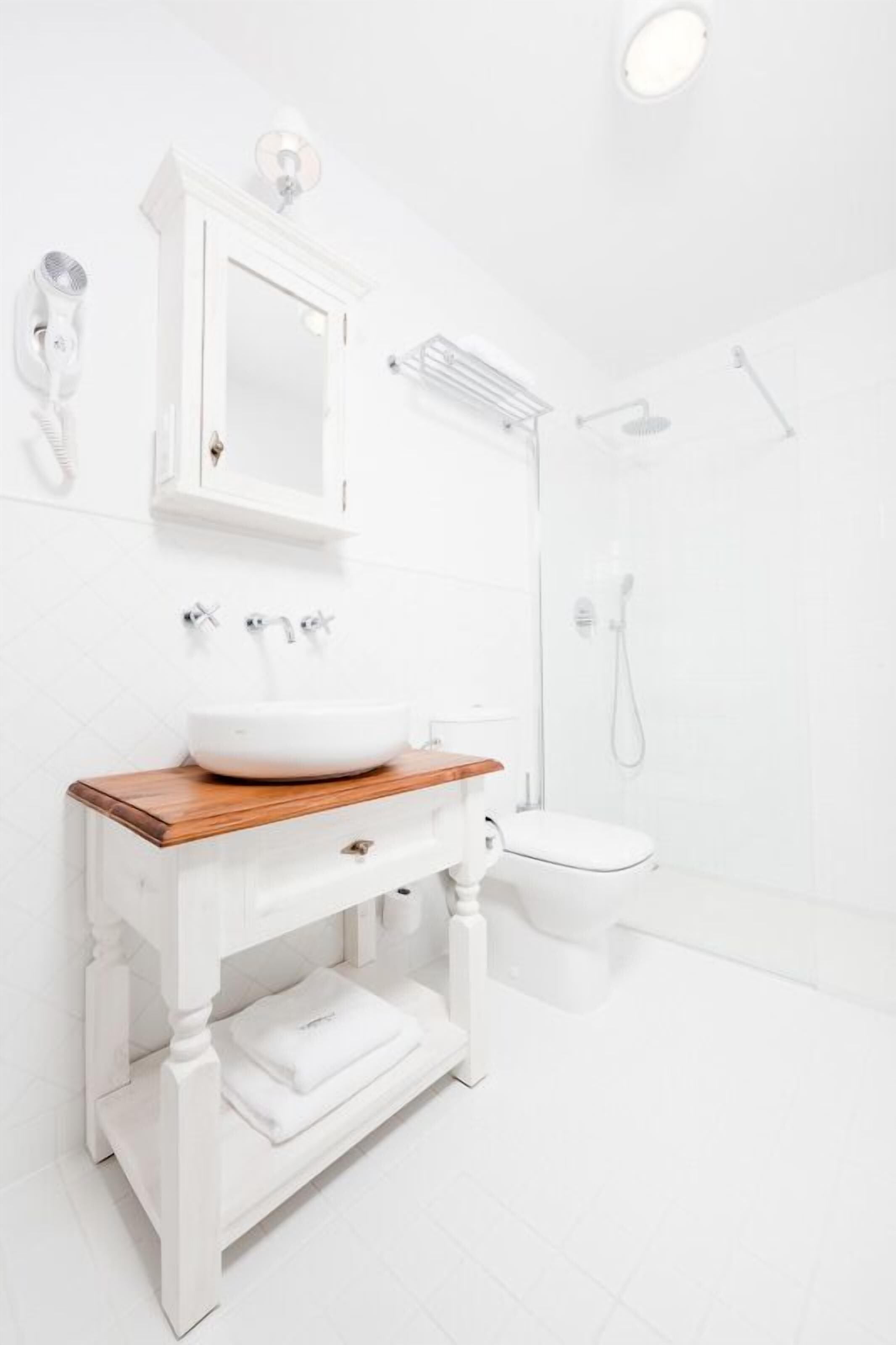 A modern bathroom with a white vanity, a wooden countertop, a white sink, a mirror, a toilet, and a shower area.