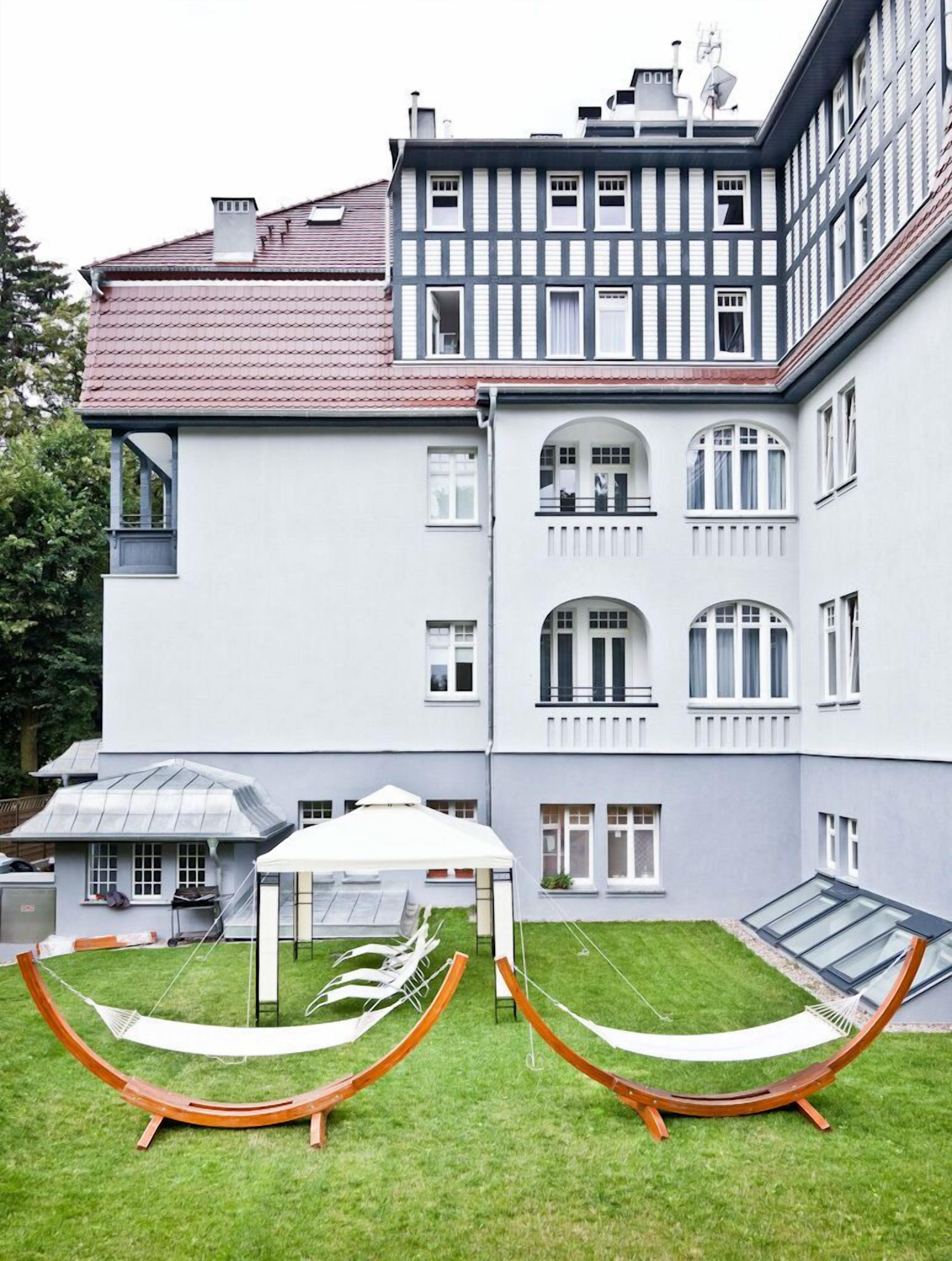 Un edificio grande de varios pisos con fachada simétrica, un patio cubierto y dos estructuras tipo hamaca al frente.