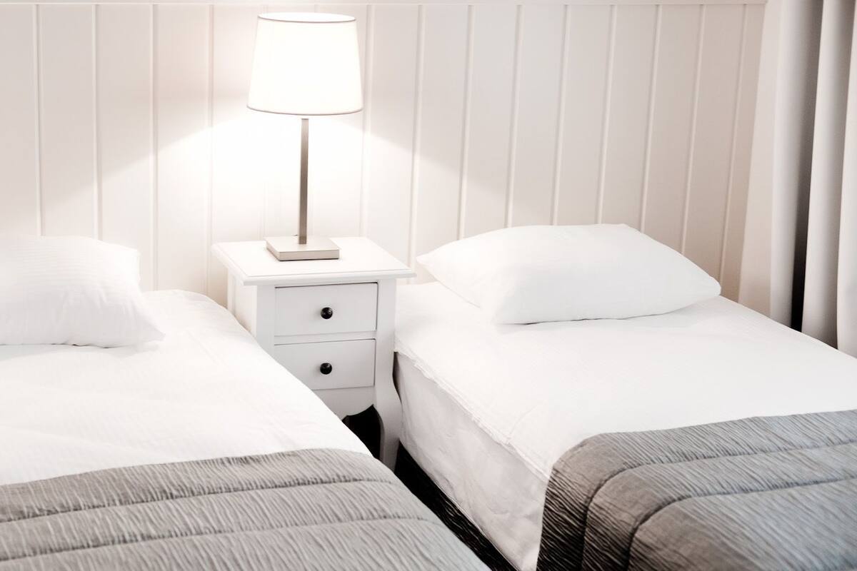 A hotel room with two single beds, a bedside table with a lamp, and a nightstand with drawers.