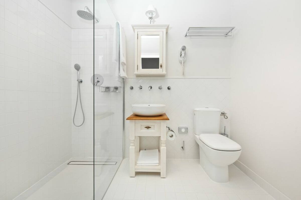 A modern bathroom with a glass shower enclosure, a white sink with a wooden countertop, a toilet, and a mirror above the sink.