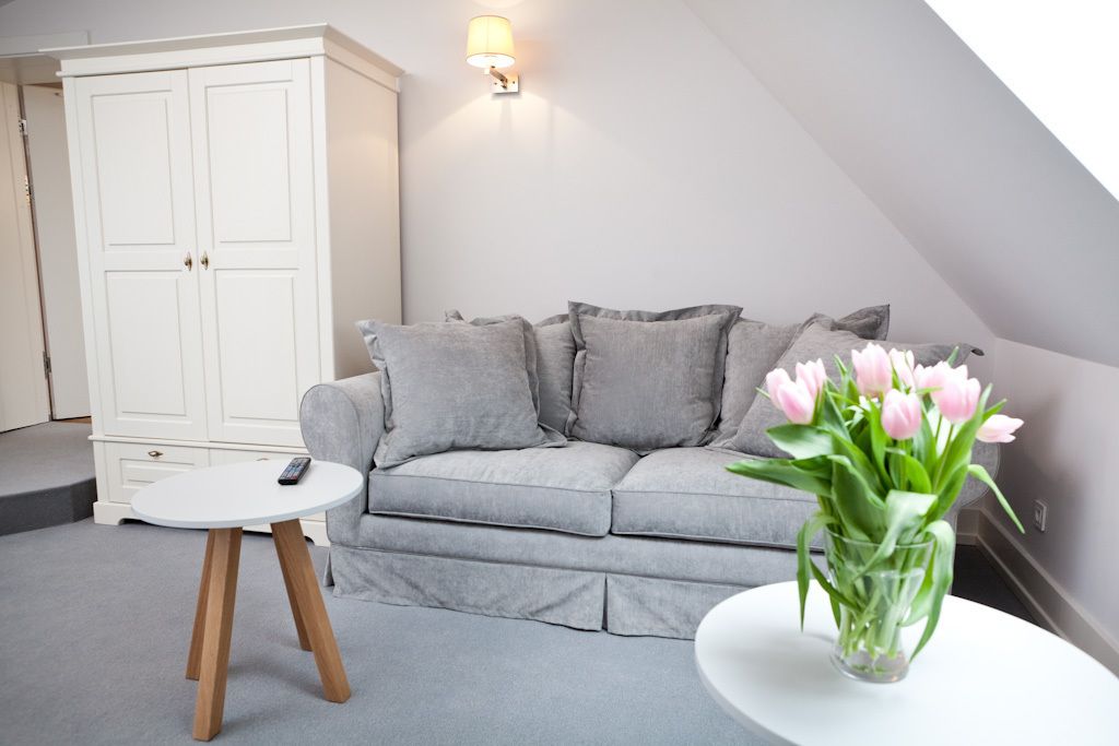 A modern living room with a grey sofa, a small round table, a white cabinet, and a vase with pink flowers.