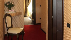 A hallway with patterned wallpaper, a red carpet, a wooden chair, a shelf with decorative items, and a door. - Domus RomAntica (Rome)