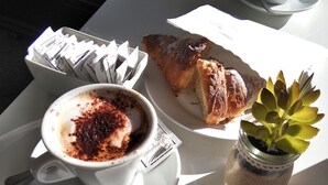 A table with a cup of coffee, a croissant, a small plant, and a packet of biscotti. - Domus RomAntica (Rome)