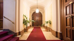 A grand hallway with a red carpet, wooden doors, and potted plants. - Domus RomAntica (Rome)