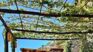 An outdoor seating area with a pergola, stone walls, and a view of the hillside.