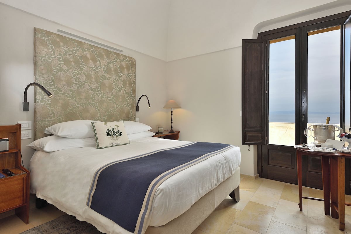 A neatly made bed with a blue and white bedspread, a bedside lamp, and a nightstand with a remote control.