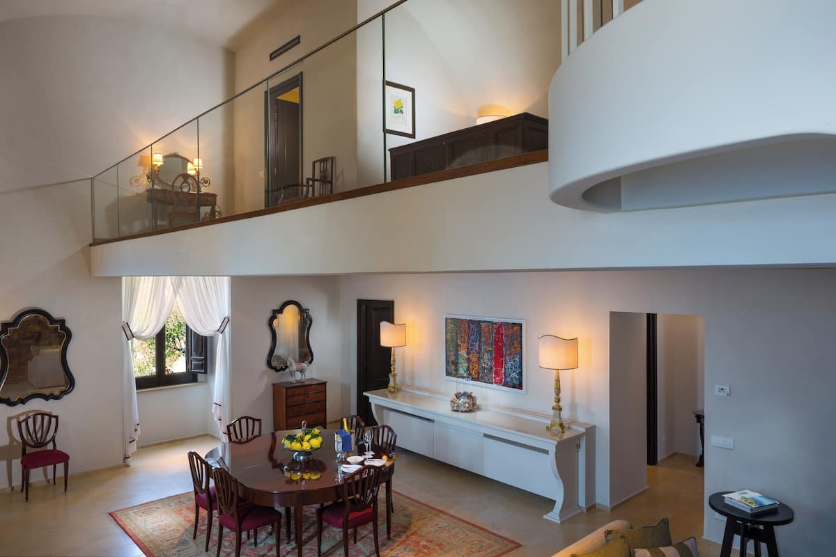 A spacious dining area with a high ceiling, a staircase, and a balcony with a railing.
