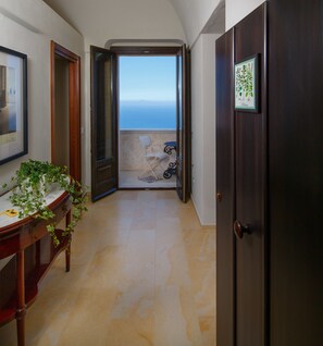 A hallway with a wooden door, a framed picture, a potted plant, and a view of the sea through an open door.