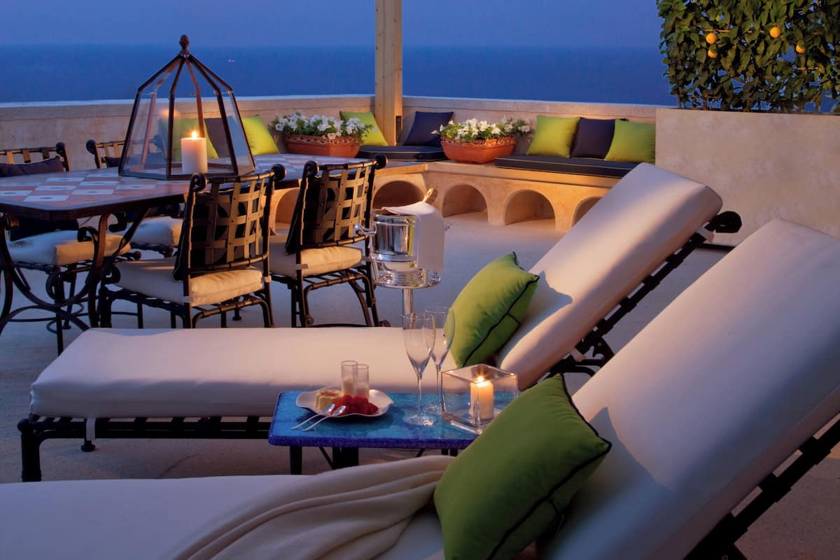 An outdoor seating area with lounge chairs, a table, and potted plants.
