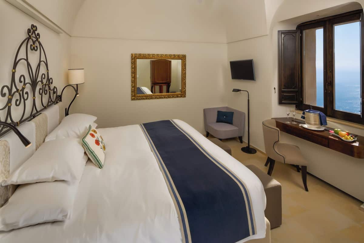 A hotel room with a bed, a desk, a chair, a TV, and a window with a view.