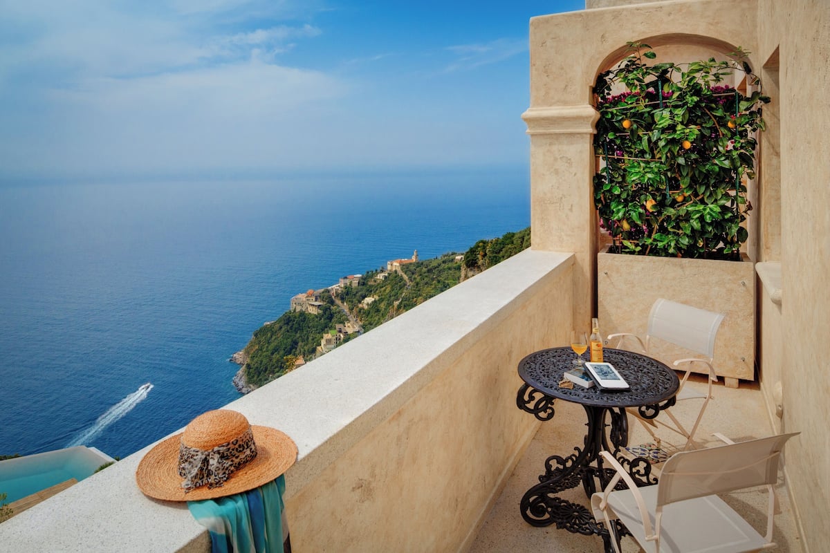 A balcony with a view of the sea, a table with chairs, and a hat on the ledge.