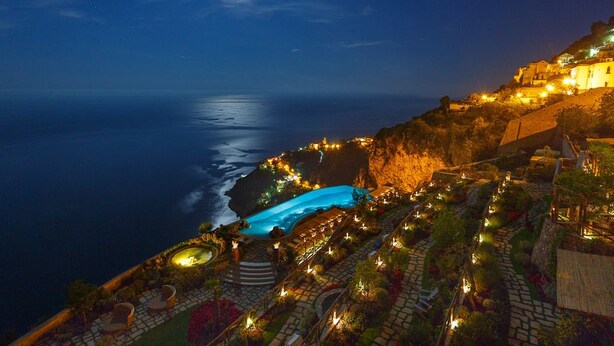 A coastal hotel with a pool, terraced gardens, and a view of the ocean.