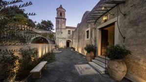 A courtyard with a stone bench, potted plants, a stone wall, and a tower in the background.
