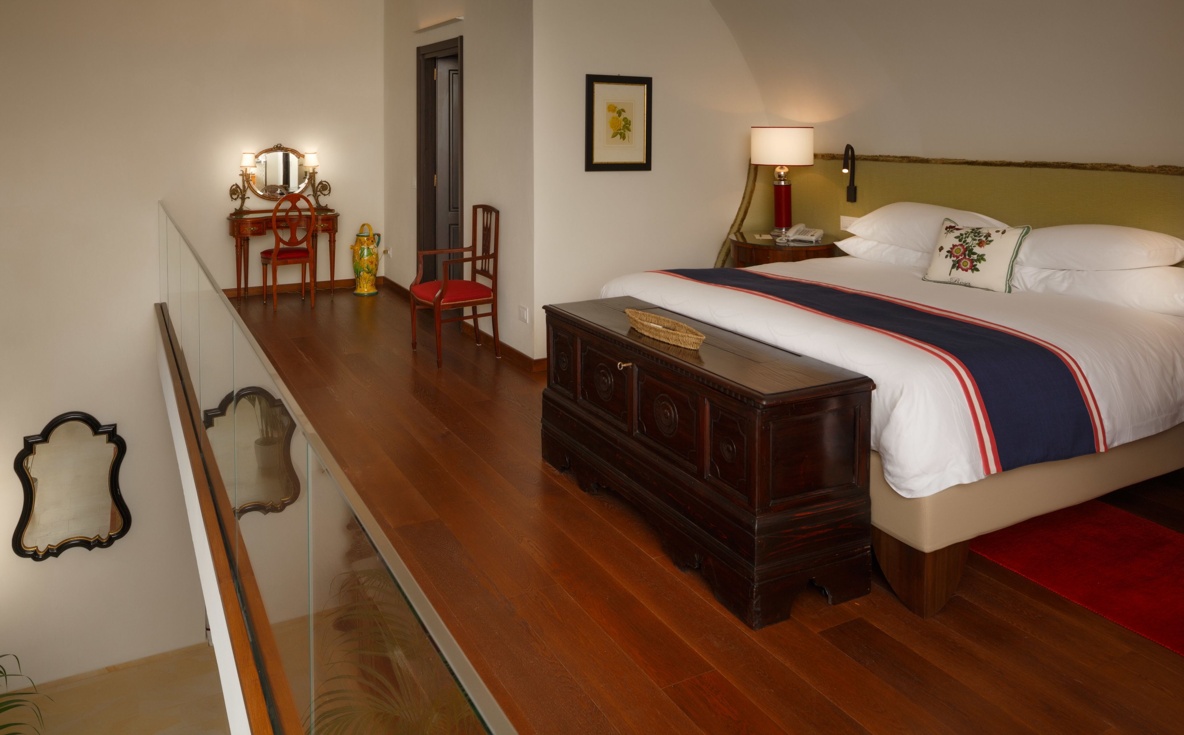 Una habitación de hotel con una cama grande, un aparador de madera, un escritorio con una lámpara y un espejo.