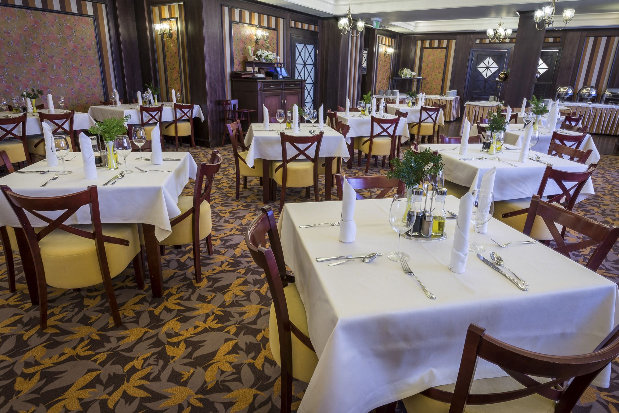 Une salle à manger élégante, avec plusieurs tables dressées pour le service, agrémentée de nappes blanches, de couverts disposés avec soin et de décorations centrales.