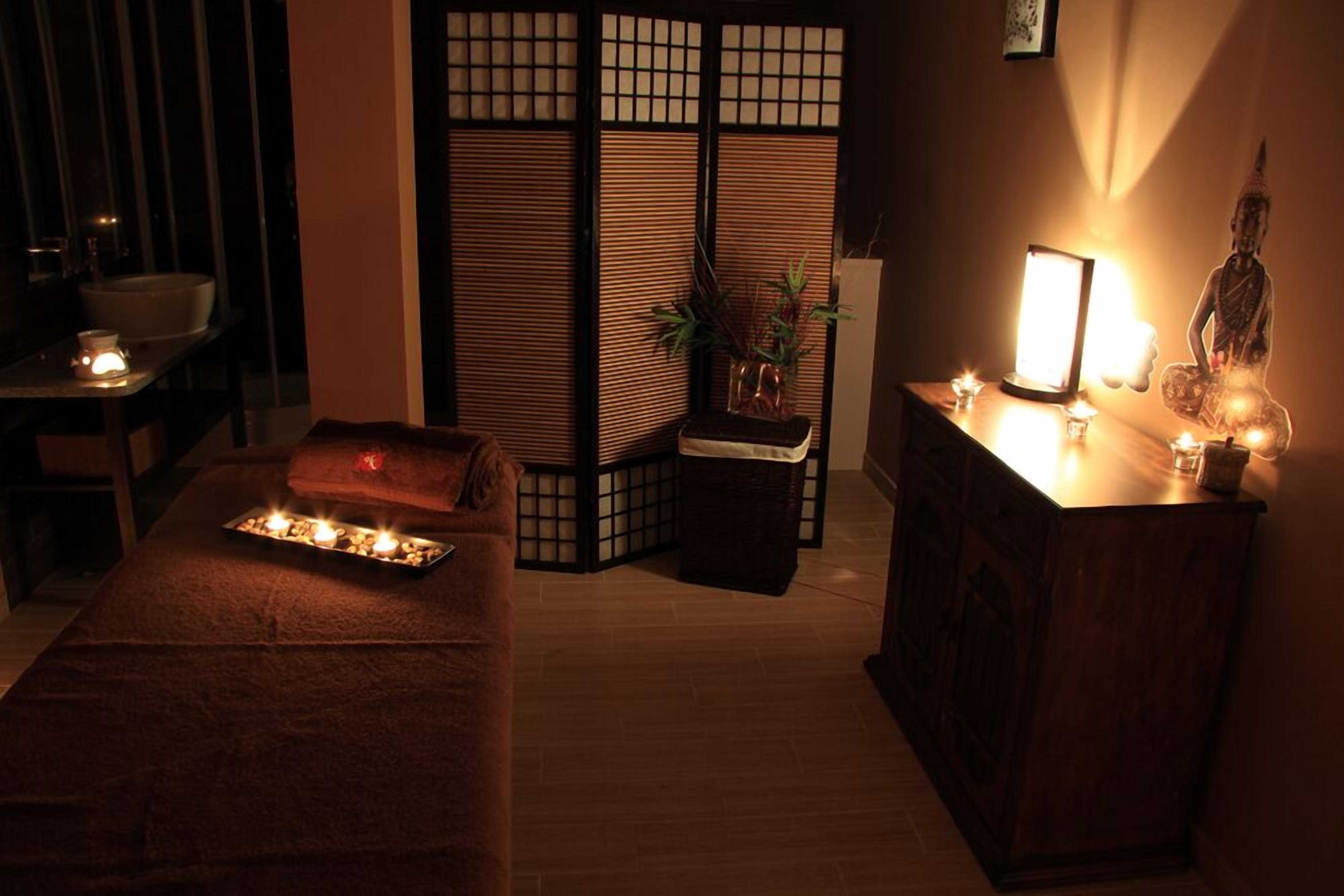A room with a massage table, a small table with candles, a Buddha statue, and a sliding door with a plant.