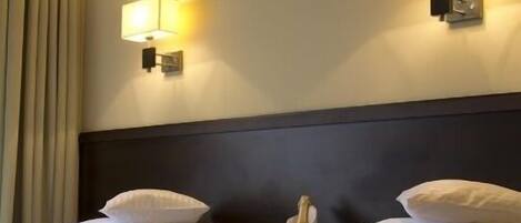 A hotel room with two beds, a headboard, and two wall-mounted lamps.