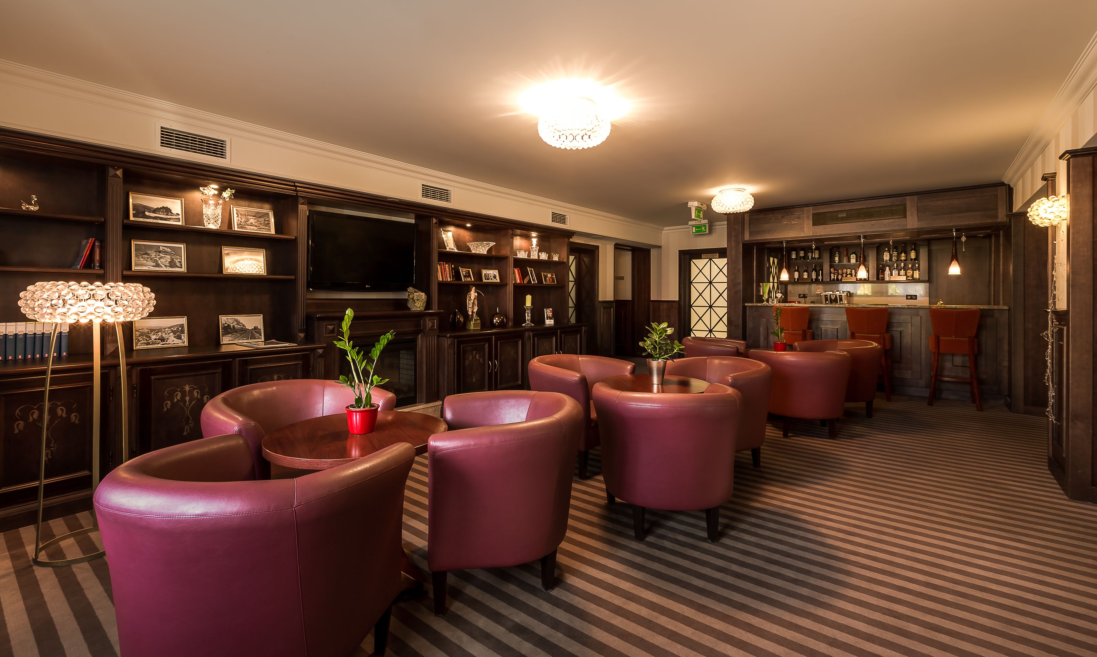 A bar area with leather chairs, a television, and a bar stocked with bottles.