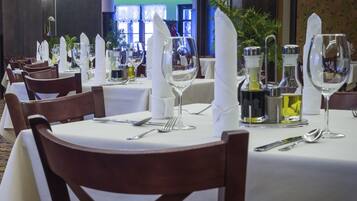 A dining area with tables set for service, featuring white tablecloths, neatly arranged cutlery, and glassware.