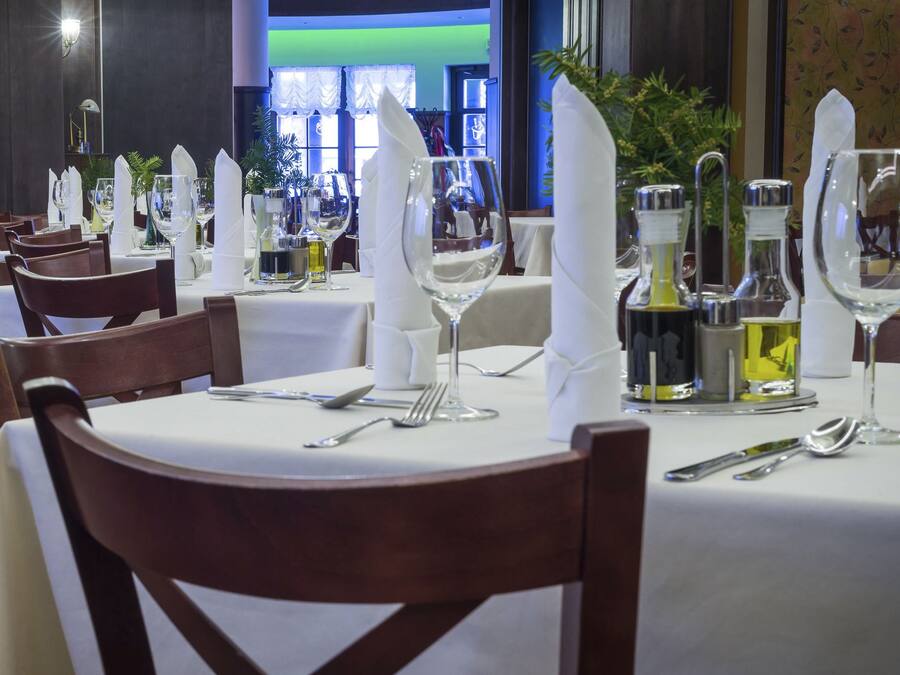 A dining area with tables set for service, featuring white tablecloths, neatly arranged cutlery, and glassware.