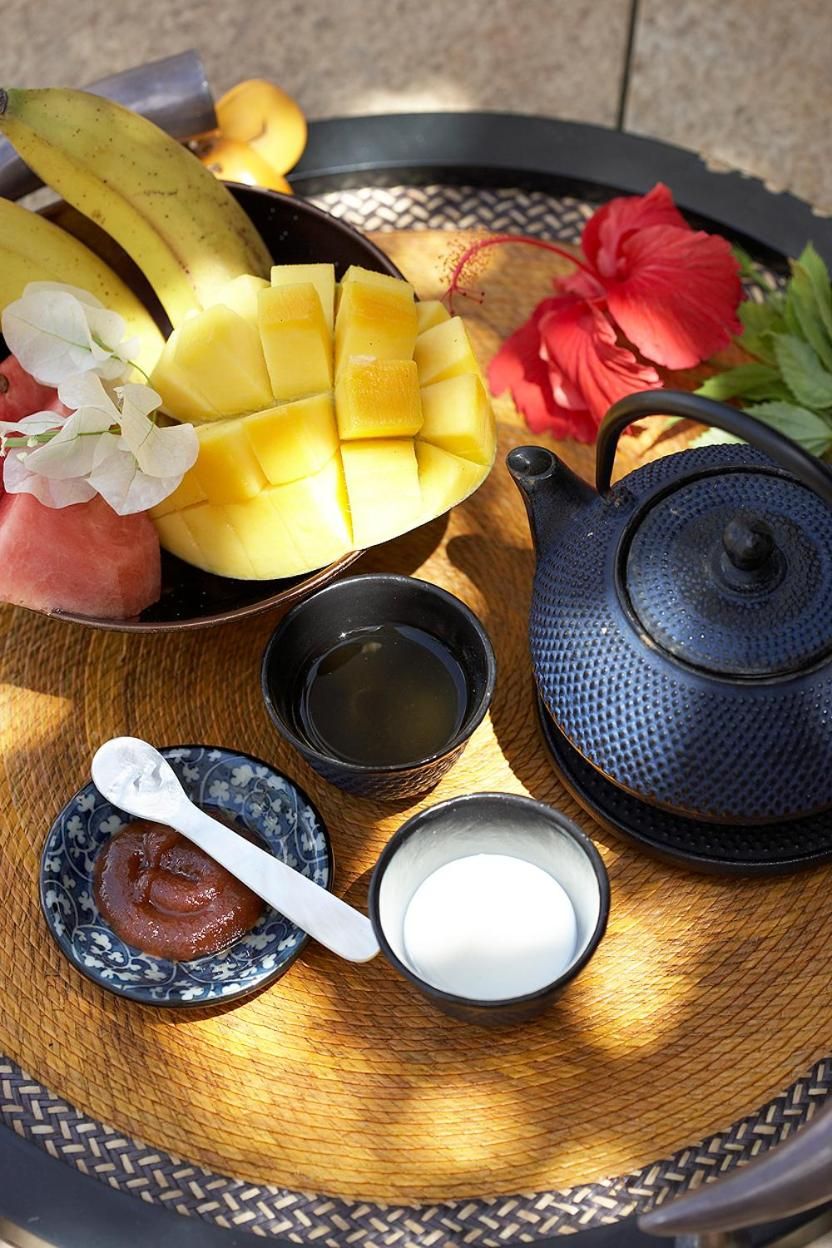 A tray with sliced mango, a teapot, a cup of tea, a spoon with jam, and a small bowl of sugar.