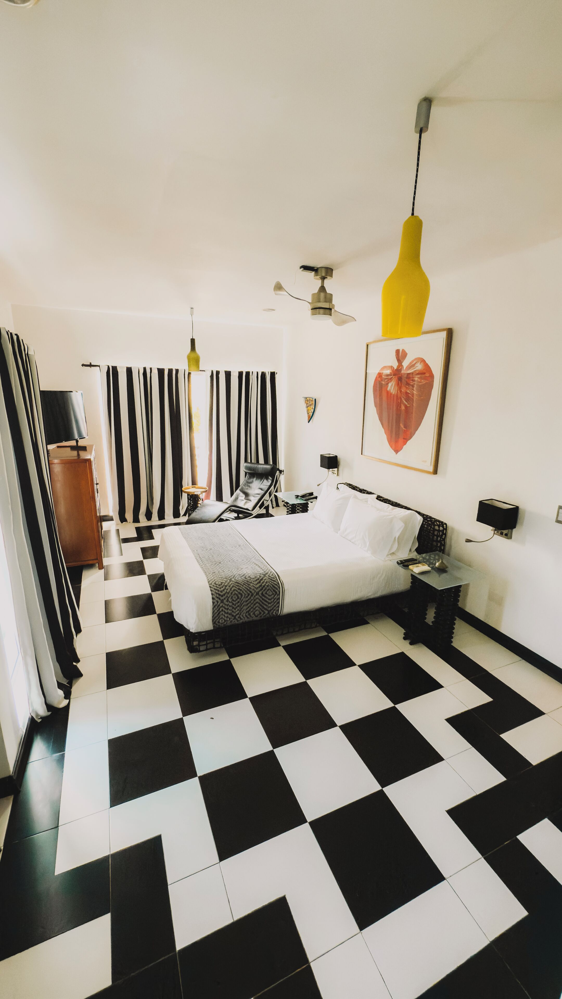 Una habitación de hotel con piso a cuadros, una cama, un escritorio, una silla, un televisor y un cuadro en la pared.