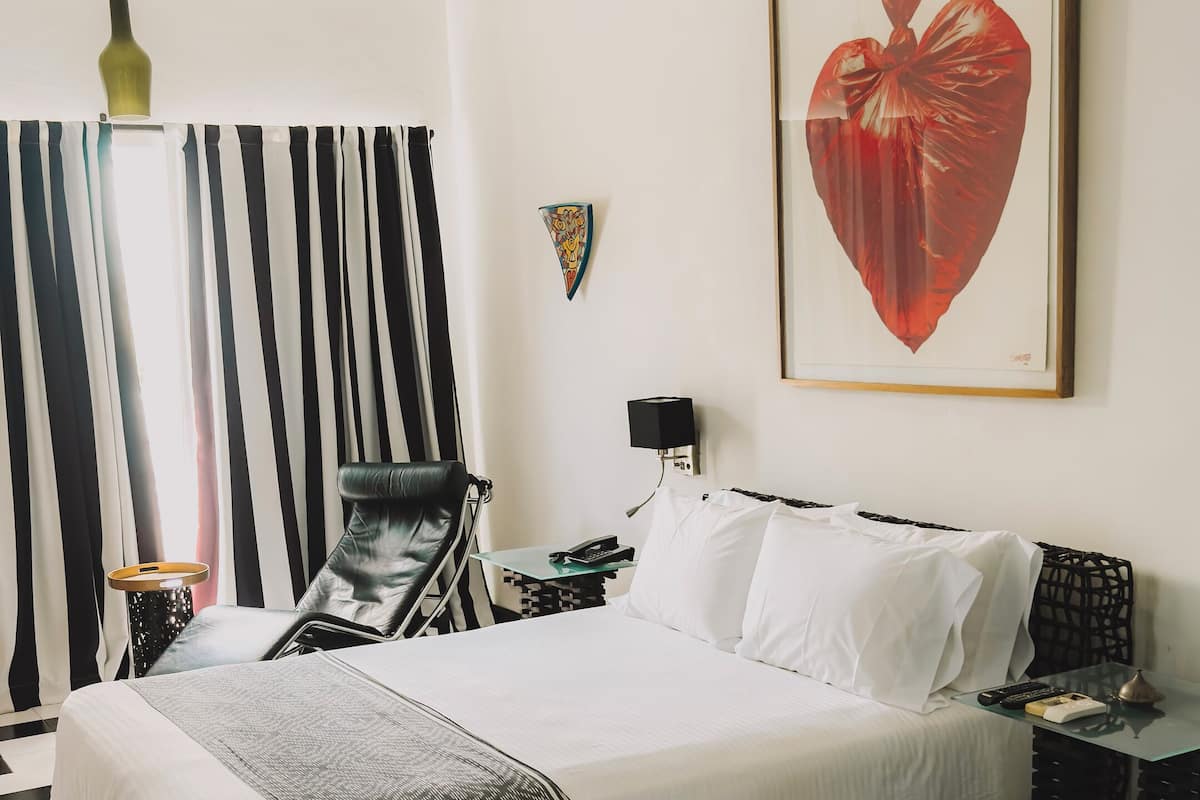 Een hotelkamer met een zwart-wit geruite vloer, een bed met witte lakens, een plafondventilator, een nachtkastje met een lamp en een lijst met een foto aan de muur.