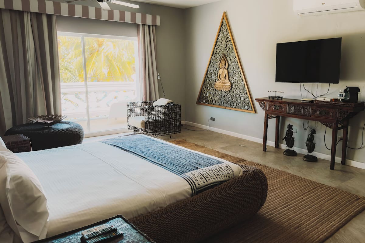 Een slaapkamer met een bed, een televisie, een decoratief wandobject en een raam met gordijnen.