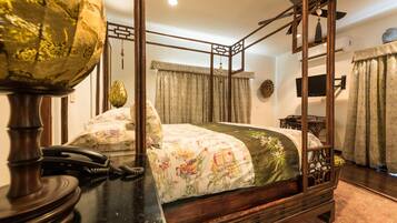 Una habitación tradicional con cama con dosel, un escritorio de madera con teléfono y un ventilador de techo.