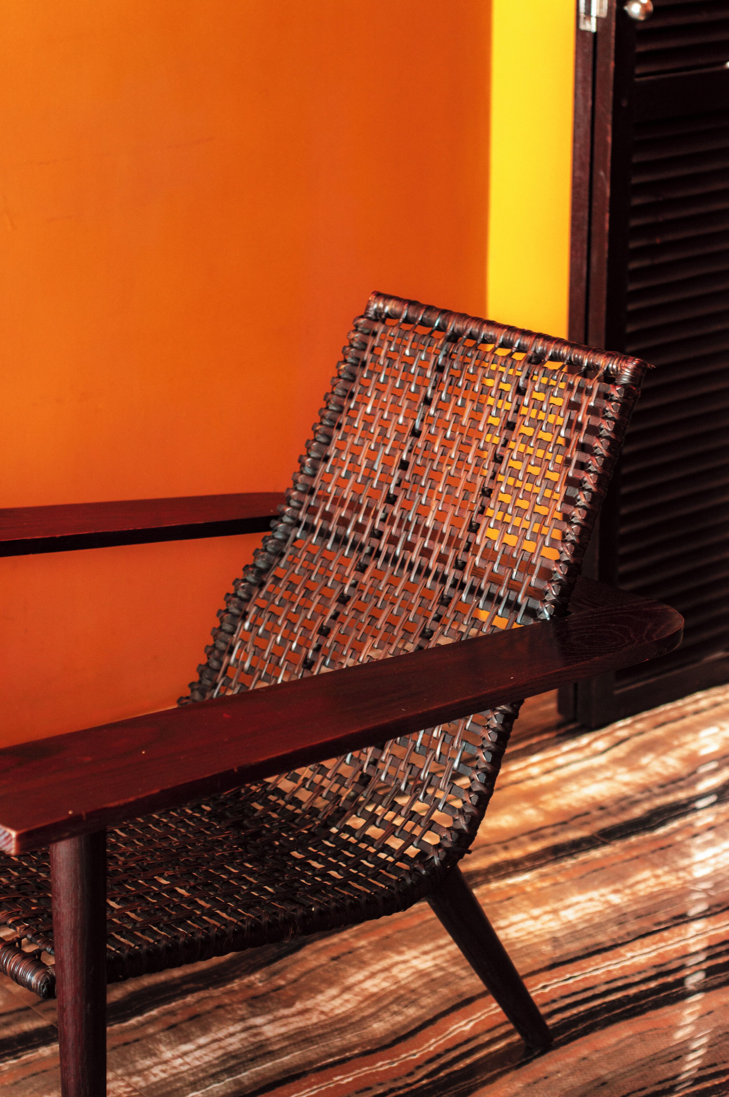Una silla con respaldo tejido y estructura de madera, ubicada frente a una pared con diseño a rayas.