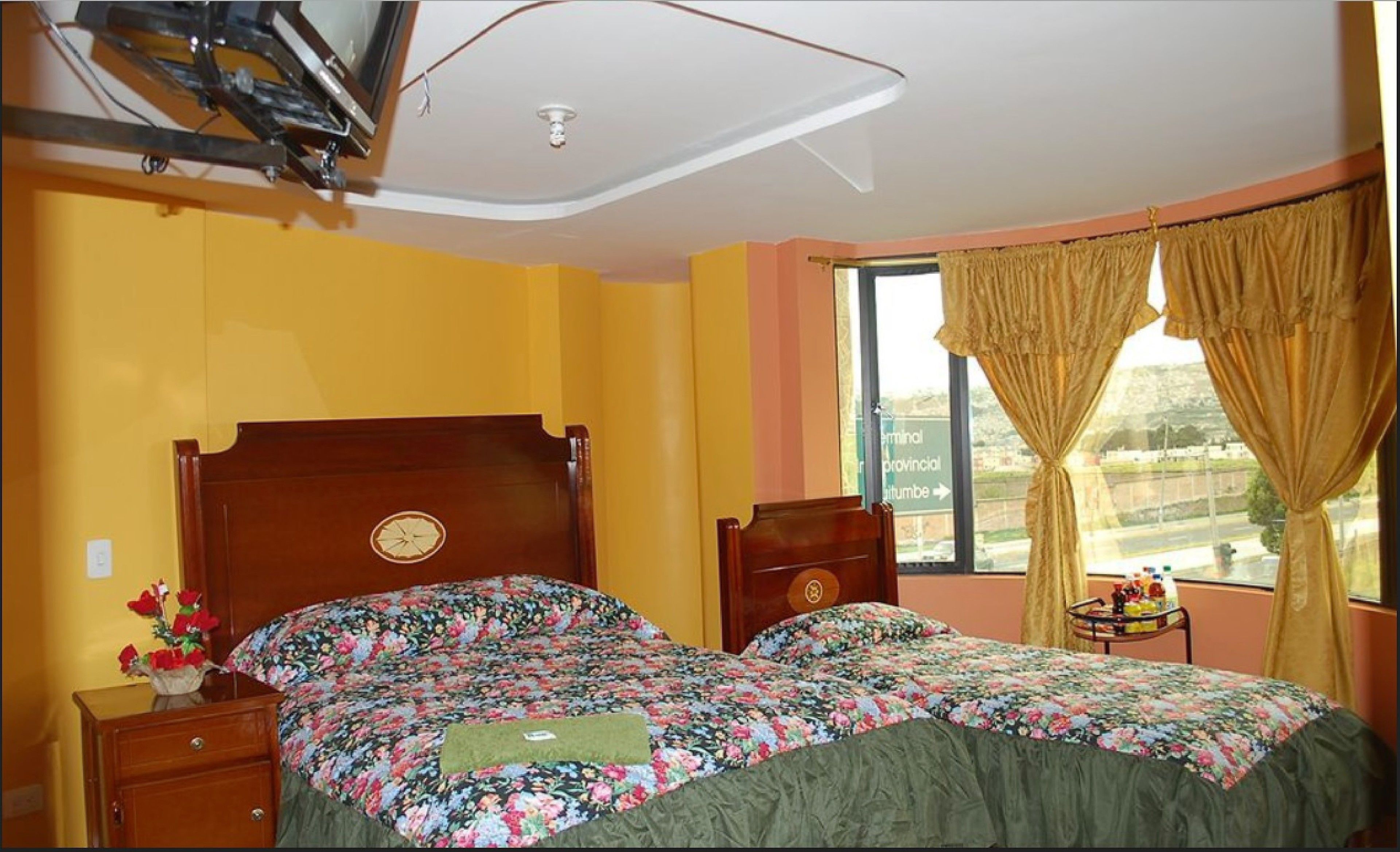 Quarto com duas camas, cabeceira de madeira, mesa de cabeceira, janela com cortinas e vista para o exterior.