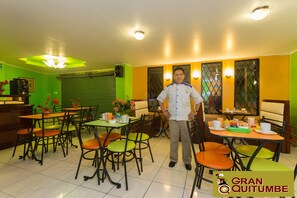 A restaurant with a chef standing, tables with chairs, and a green and yellow color scheme. - Hotel Gran Quitumbe (Quito)