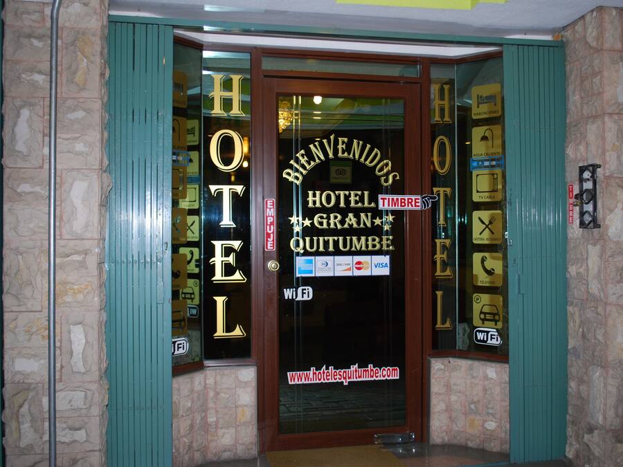 A hotel entrance with a glass door displaying "BIENVENIDOS HOTEL GRAN QUITUMBE" and amenities like Wi-Fi, TV, and phone.