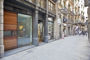 A street with shops, including a visible storefront with a large glass window and a wooden door. - Inspired by EnjoyApartments (Barcelona)